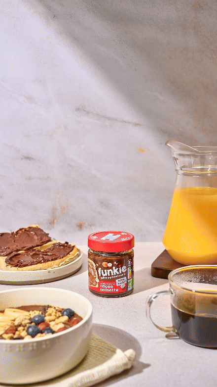 Petit-déjeuner avec tartines au chocolat, pot de pâte à tartiner, pichet de jus d'orange, bol de fruits avec granola et tasse de café.