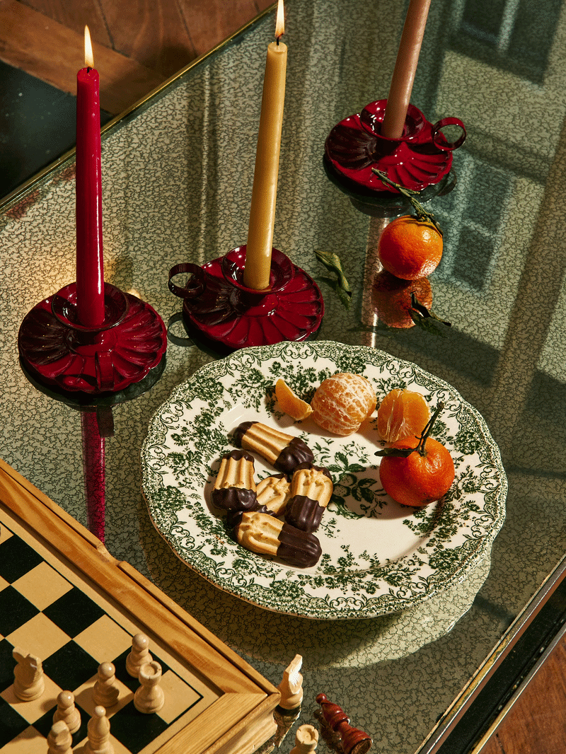 Une table avec des bougies allumées, des mandarines, des bonbons, une plaque d'échecs en bois et des objets décoratifs en verre rouge.