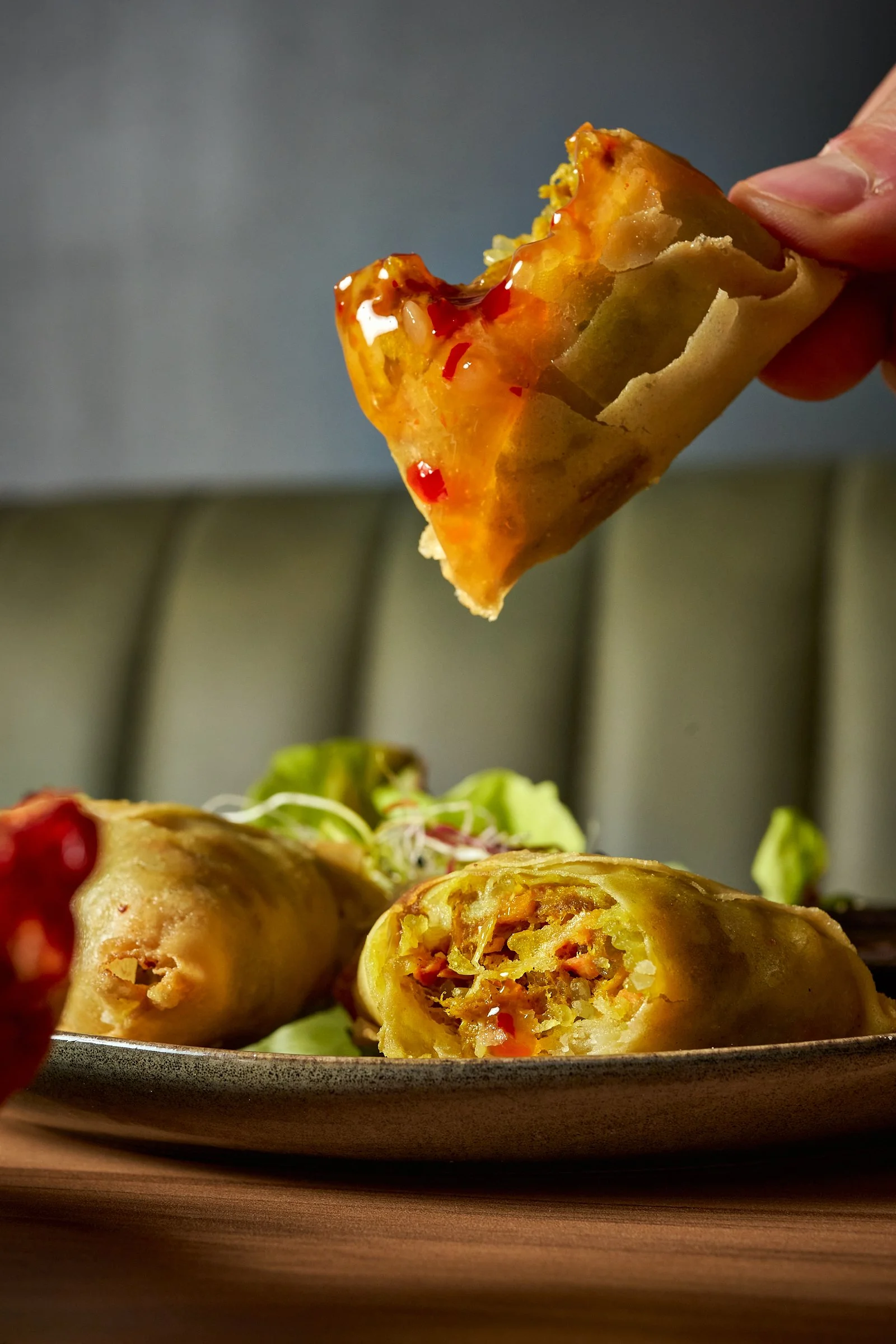 Une personne tient un rouleau de printemps coupé en deux avec une garniture de légumes visibles, posés sur une assiette avec une salade verte en arrière-plan.