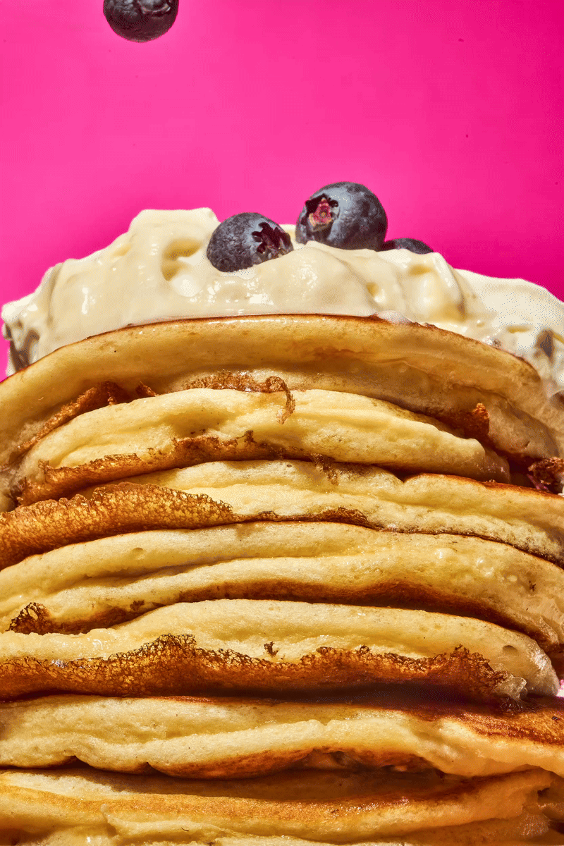 Pile de pancakes avec crème et myrtilles sur fond rose.