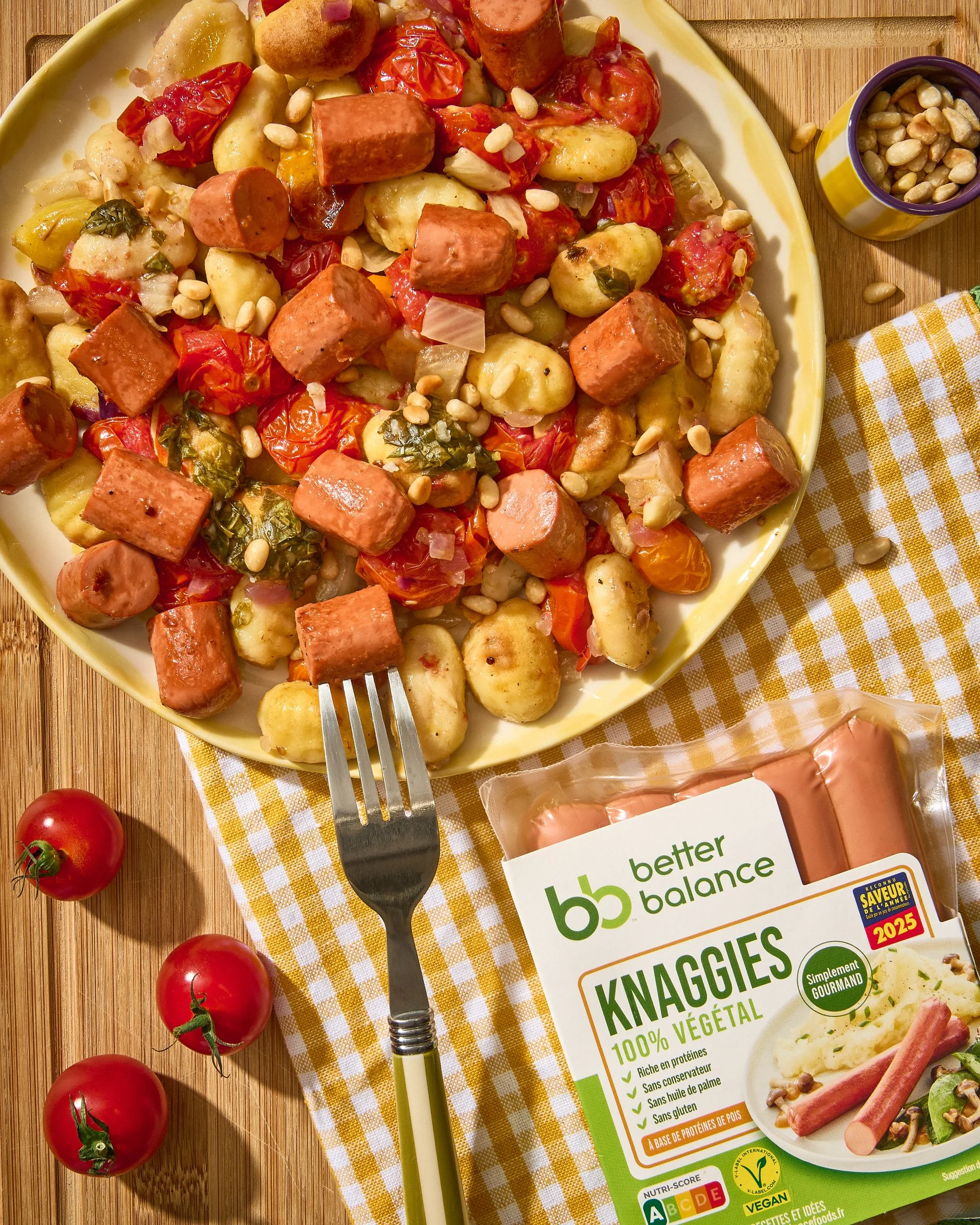 Une assiette de gnocchis végétariens avec des saucisses végétales, des tomates cerises, de l'ail, et des graines, avec une boîte de gnocchis Better Balance et des tomates sur la table.
