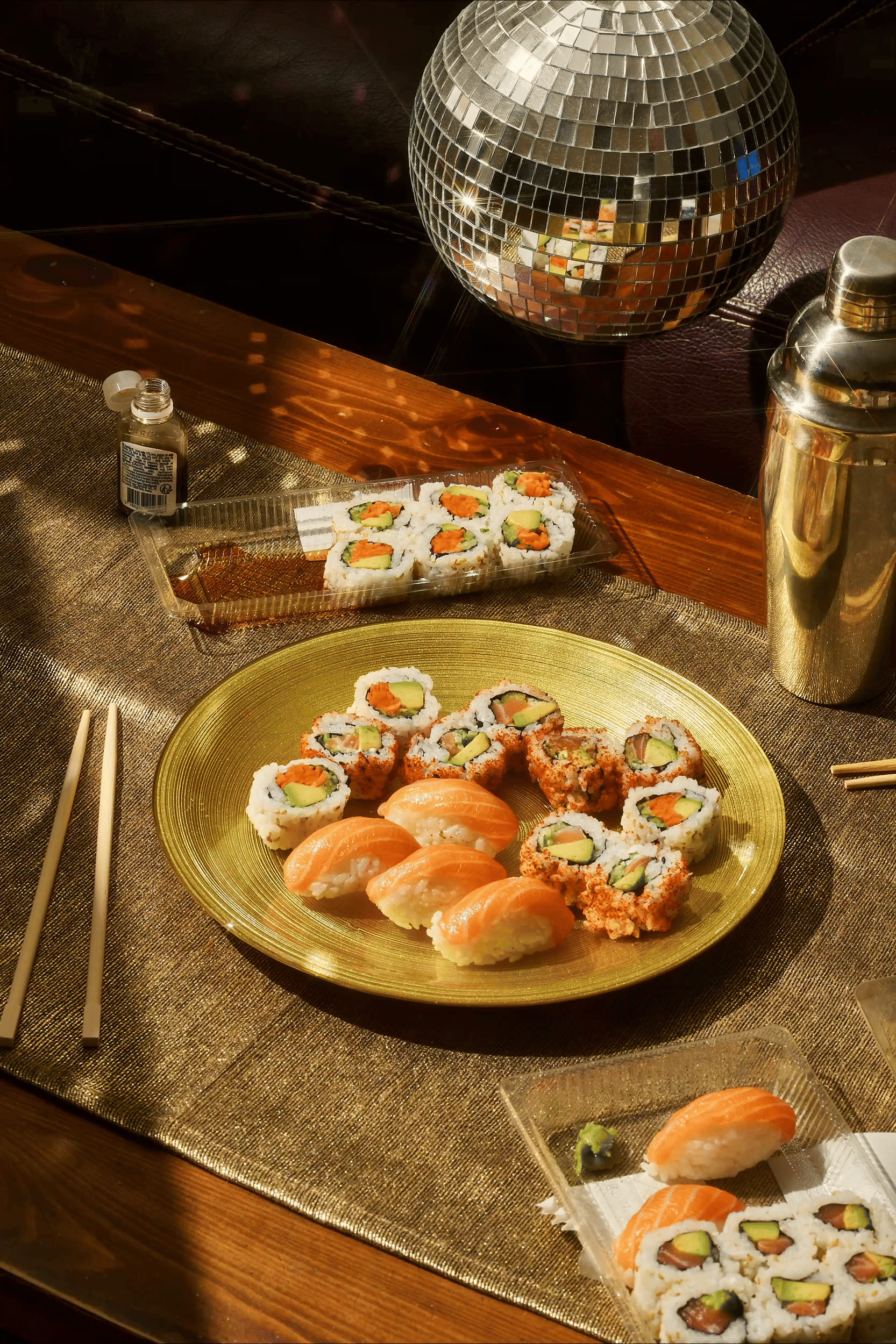 Plateau de sushis et makis, boule disco, shaker, sauce soja et baguettes sur une table.