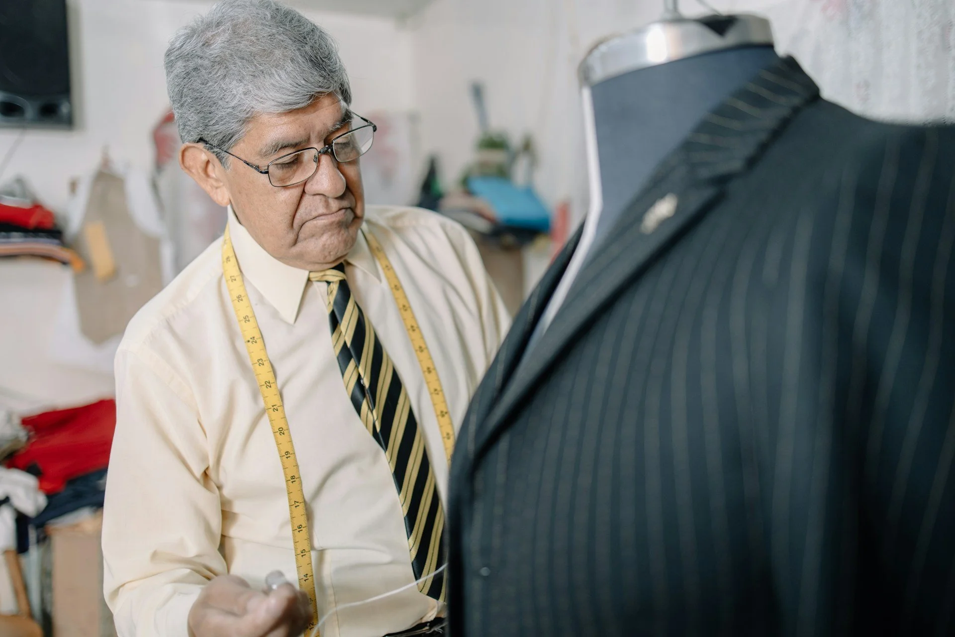 a tailor wearing a measuring tape around his neck while he makes adjustments to a mannequin