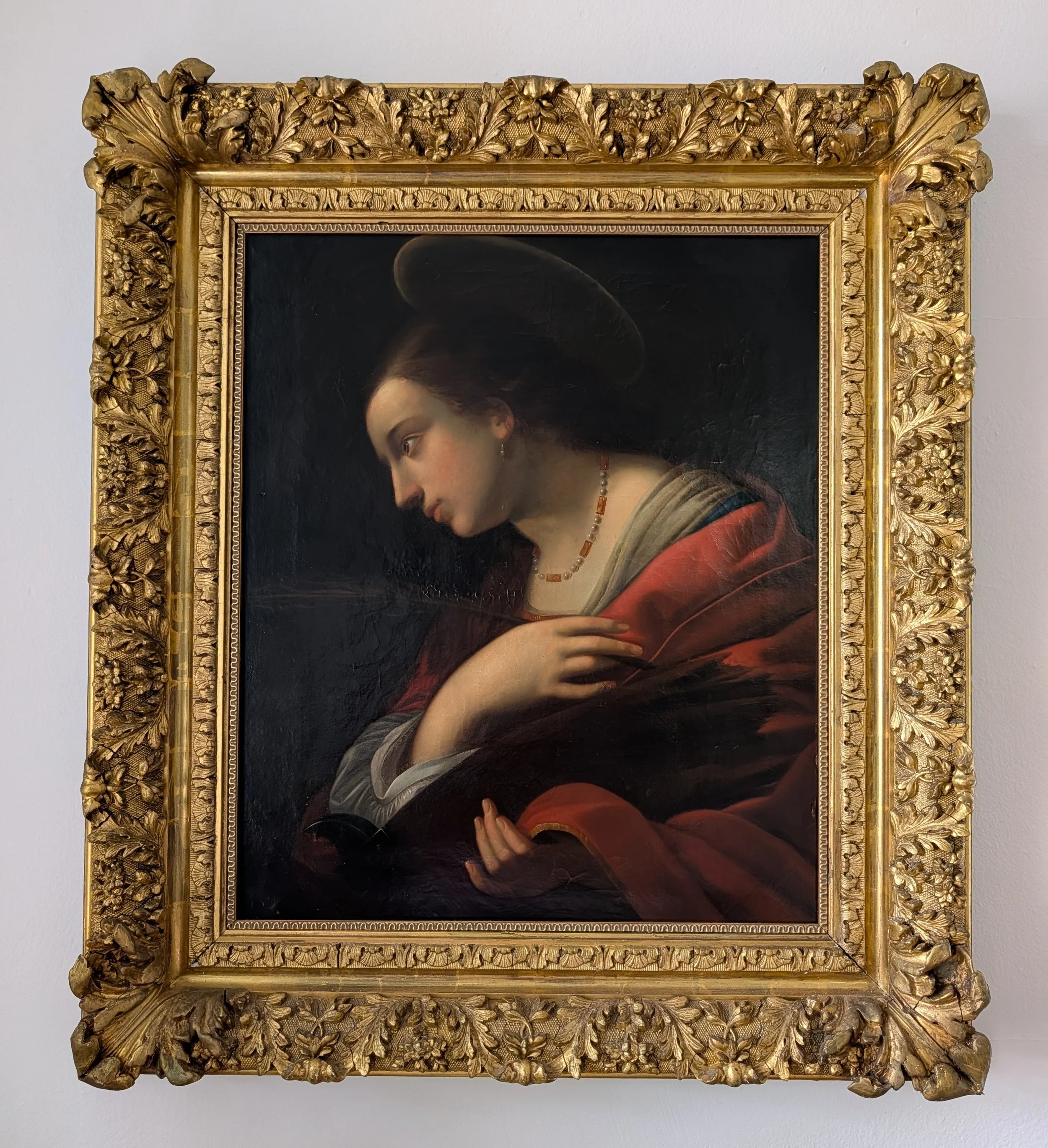 A classical portrait painting of a woman with dark hair in a bun wearing a dark hat, pearl necklace, and elegant clothing, framed in ornate gold decor.