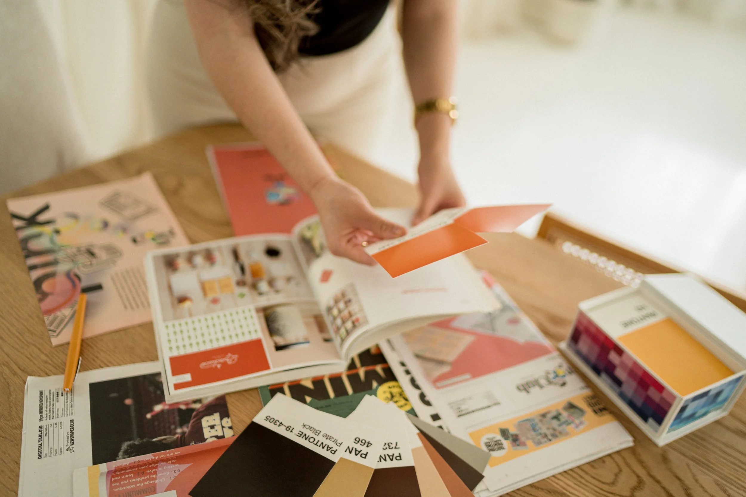 Person flipping through colorful magazines and color swatches on a wooden table.