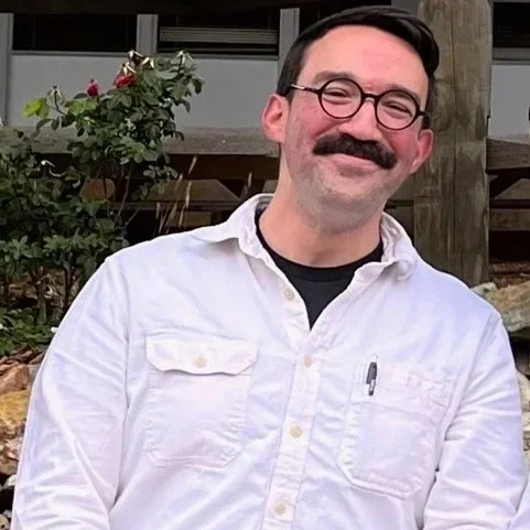 white man with white shirt, black glasses and brown mustache