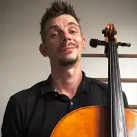 White man with short hair and goatee smiling and holding a cello.