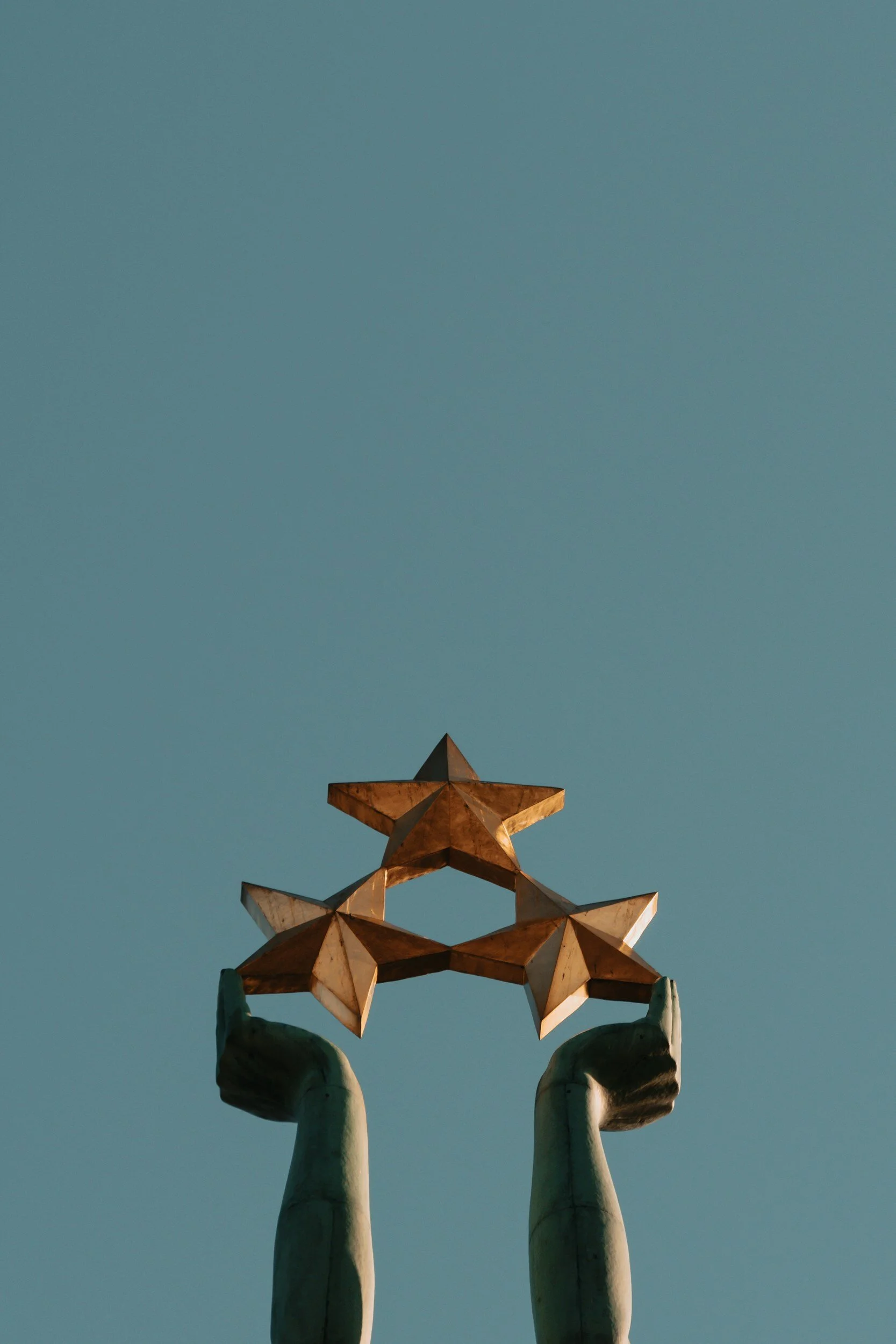Two hands raising golden stars against a clear sky.