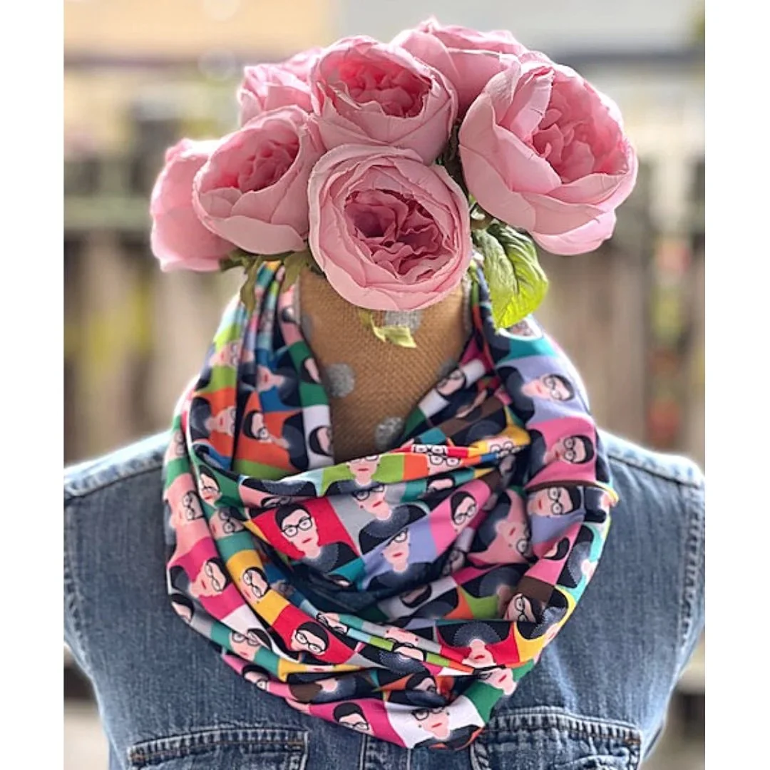 A mannequin with pink roses as a head, wearing a colorful patterned scarf featuring cartoon faces, and a denim jacket.