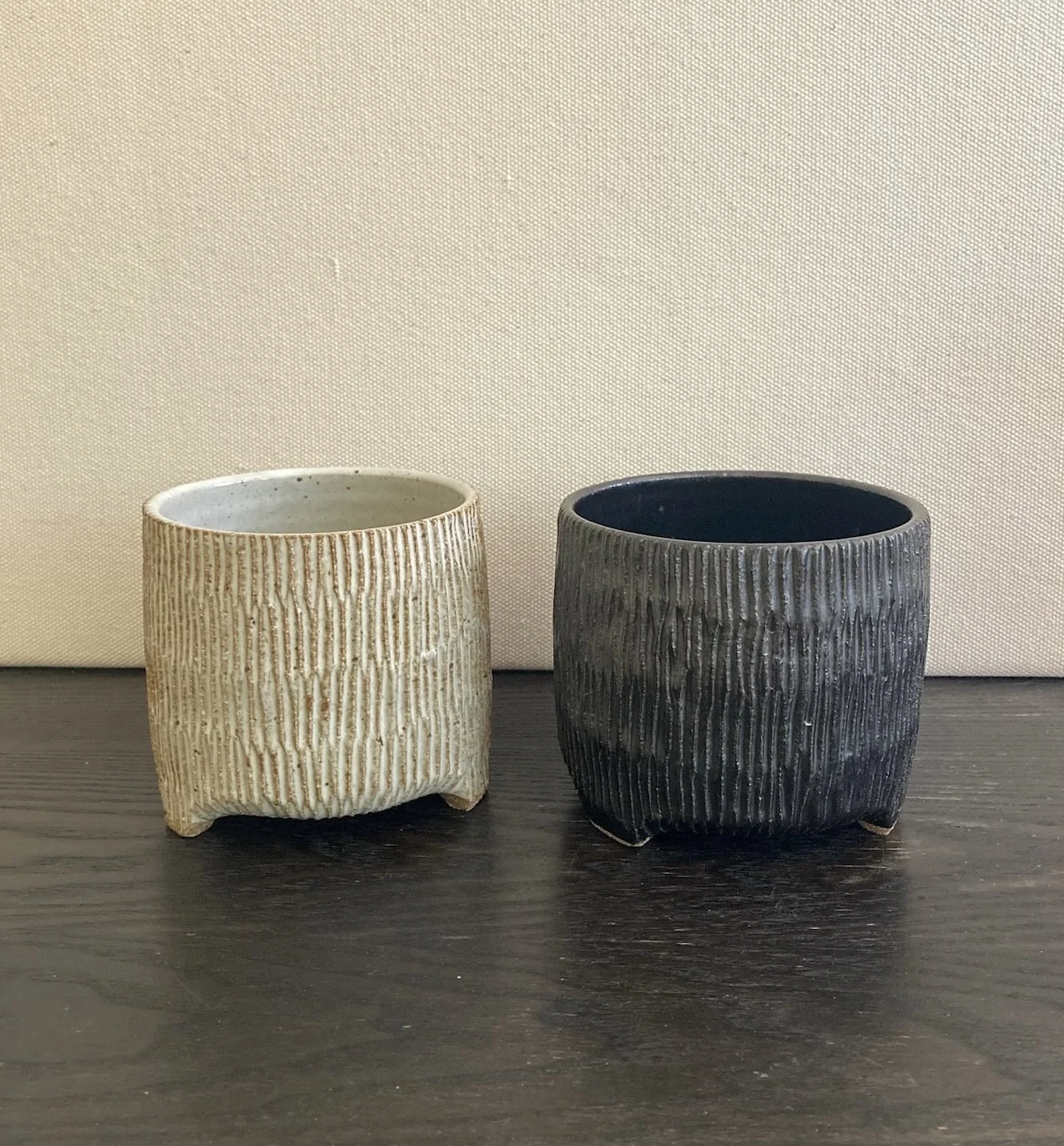 Two textured ceramic pots, one beige and one dark gray, on a dark wooden surface.