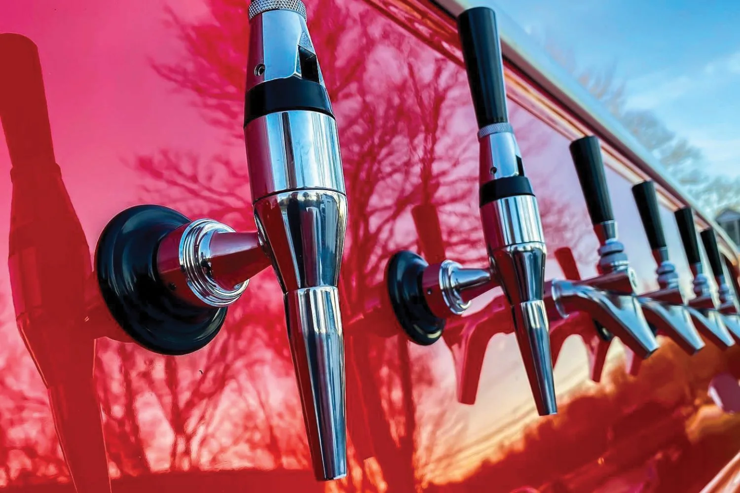 Close-up of multiple chrome and black beer taps with blue tips on a red vintage Chevrolet mobile bar.