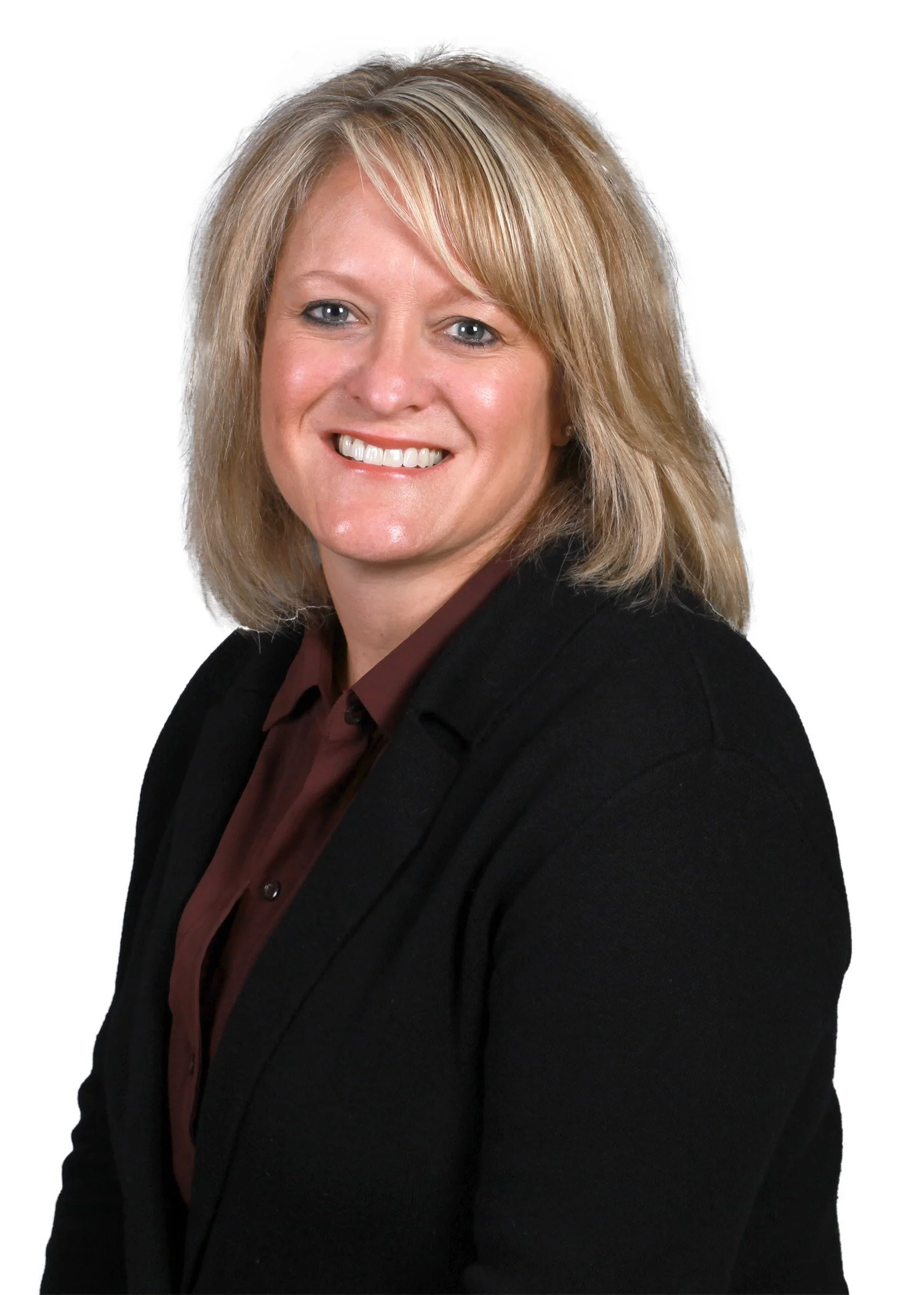 A woman with blonde hair and blue eyes smiling, wearing a black blazer and a dark red shirt, against a white background.