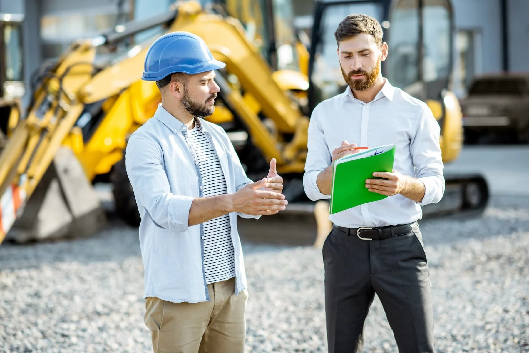 Two men discussing in front of construction equipment.