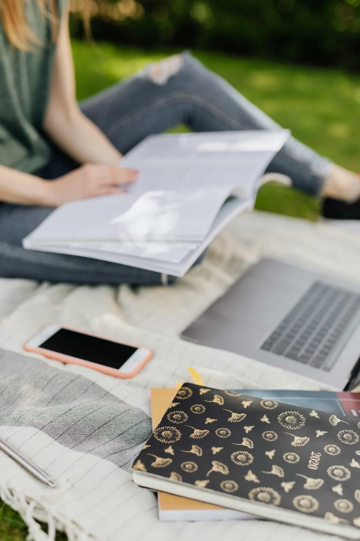 Female student on a blanket studying on a campus lawn with books and laptop