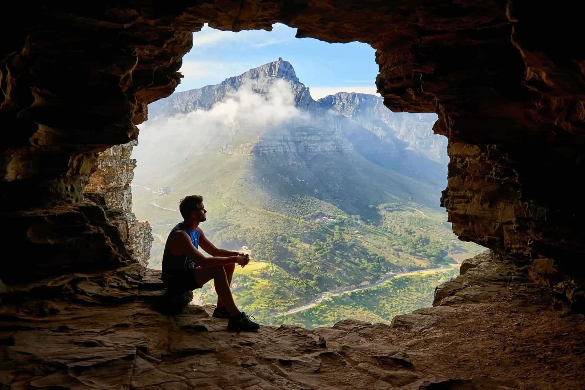 man sitting in a cave overlooking the mountains