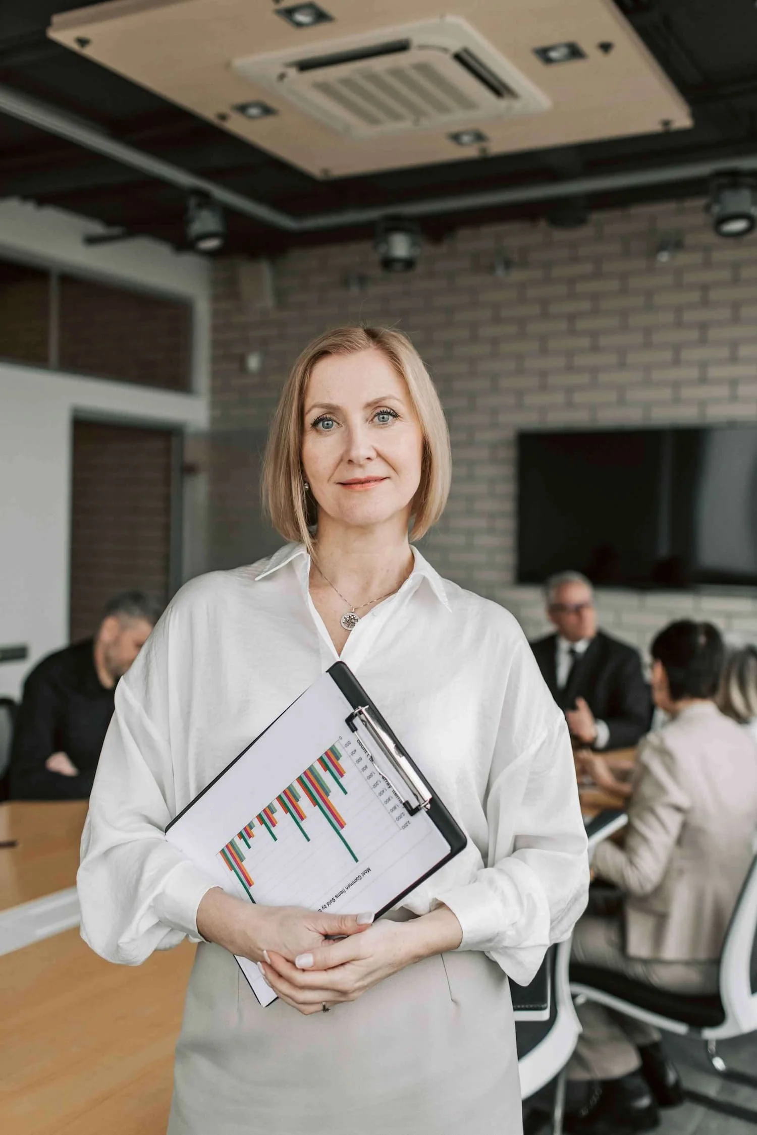 Female manager smiling at camera while holding a clipboard report.