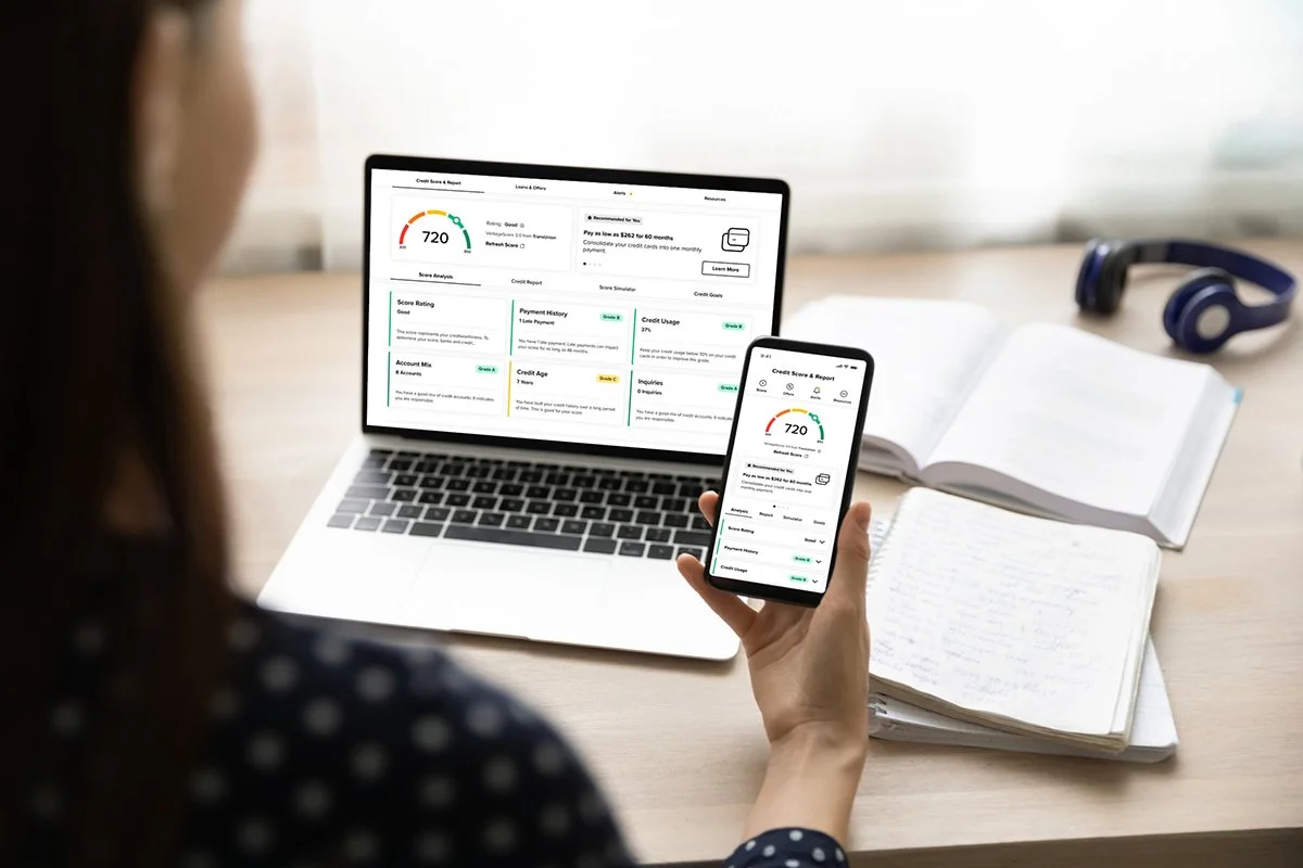 Women holding a phone with a laptop open in the background both screens has her credit report