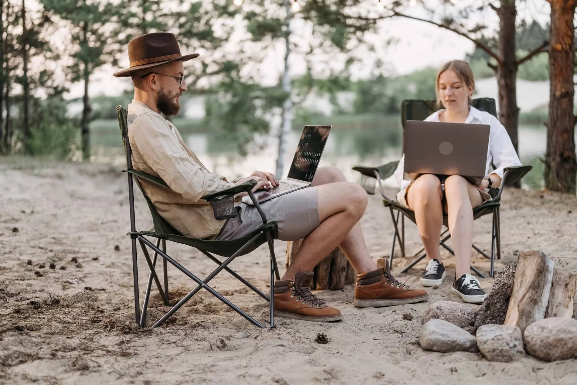 a man and woman sitting in foldable chairs outside on their laptop