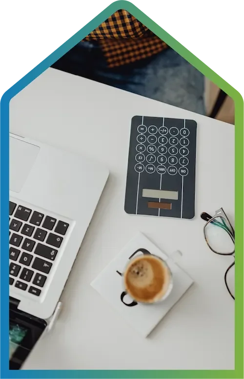 A desk view of a computer, calculator, glasses, and coffee.