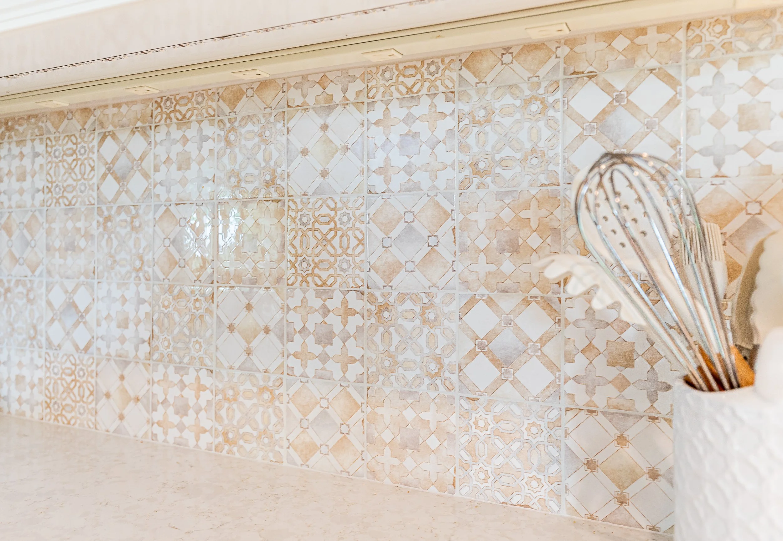 Decorative beige and white patterned tiles on a kitchen wall with a container holding cooking utensils.