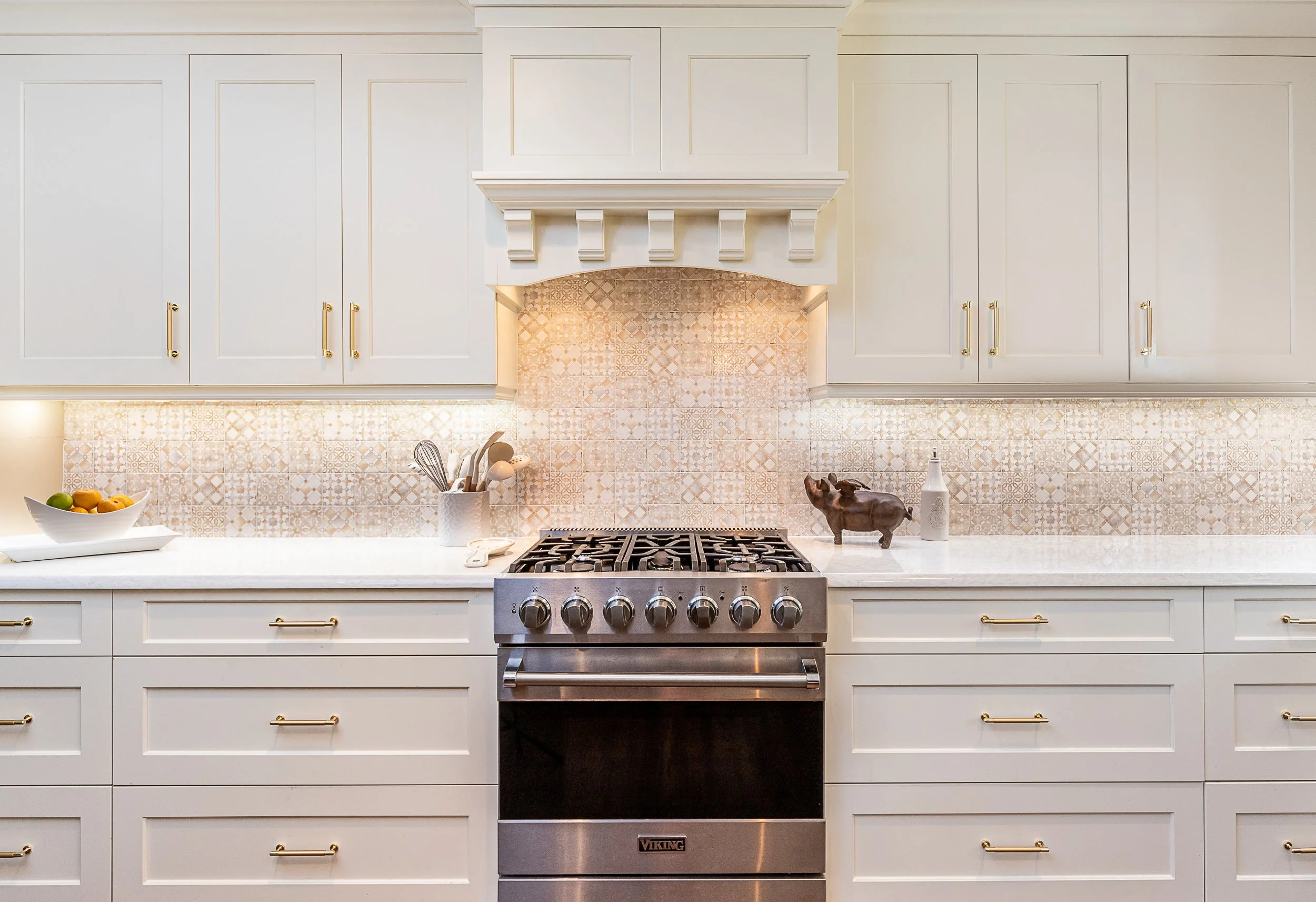 Modern kitchen with beige cabinets, a stainless steel Viking oven, decorative ceramic backsplash, and kitchen utensils on the counter.