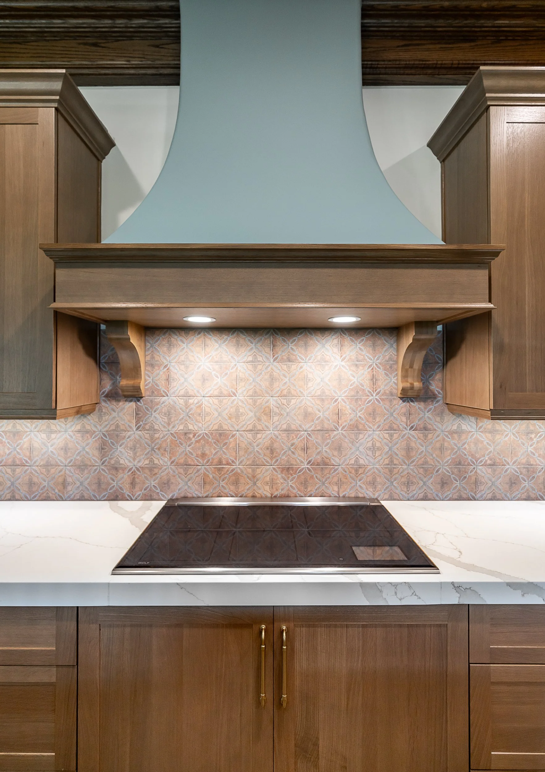 Kitchen with wooden cabinets, patterned tile backsplash, a black induction cooktop, and a white marble countertop.