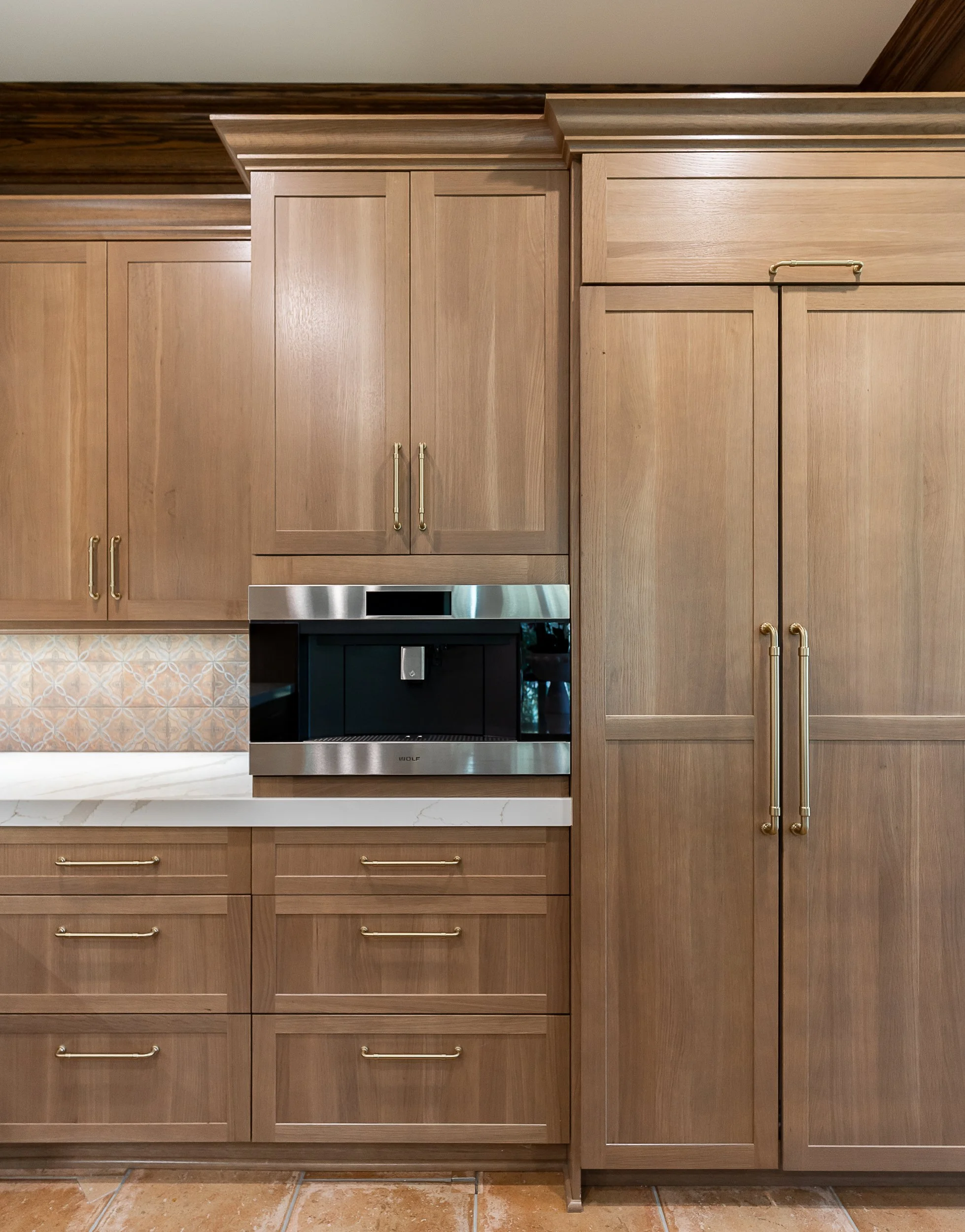 Kitchen cabinets with brass handles, a built-in microwave oven, and tile flooring.