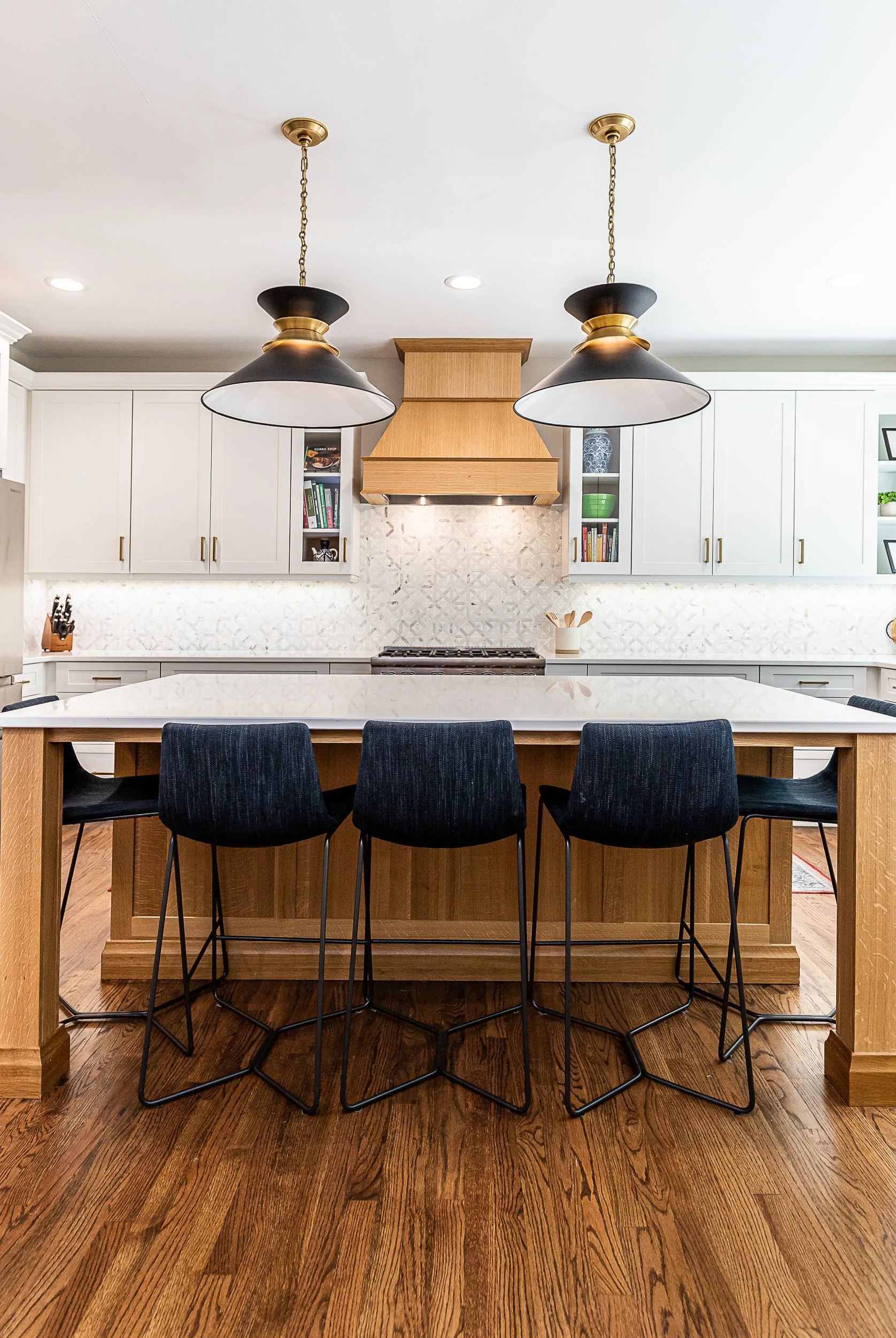 A modern kitchen with white cabinets, a central island with a quartz countertop, dark blue barstools, and two black pendant lights hanging from the ceiling.