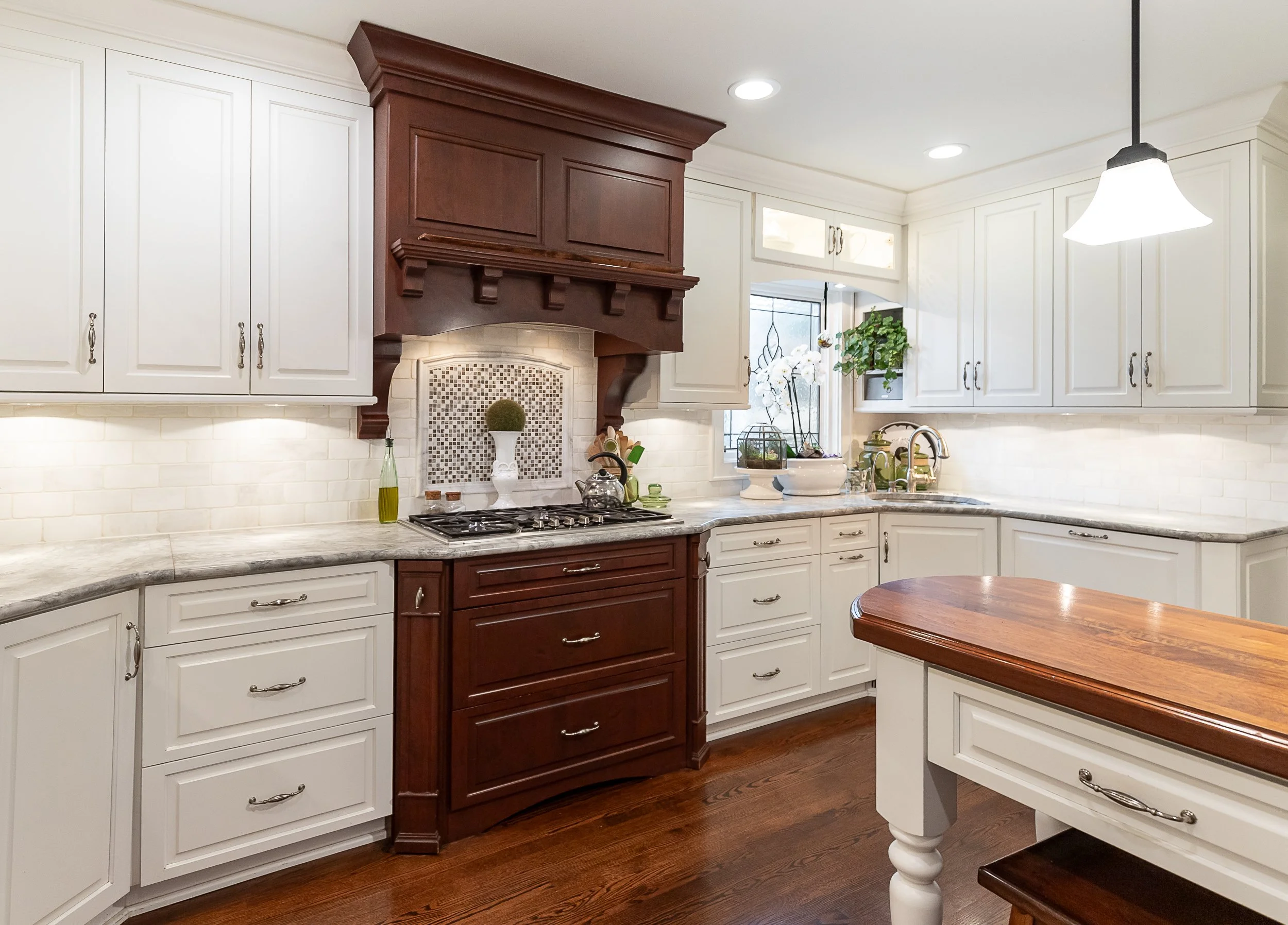 A bright kitchen with white cabinets, a dark wood range hood, a quartz countertop, and a center island with a wooden top.