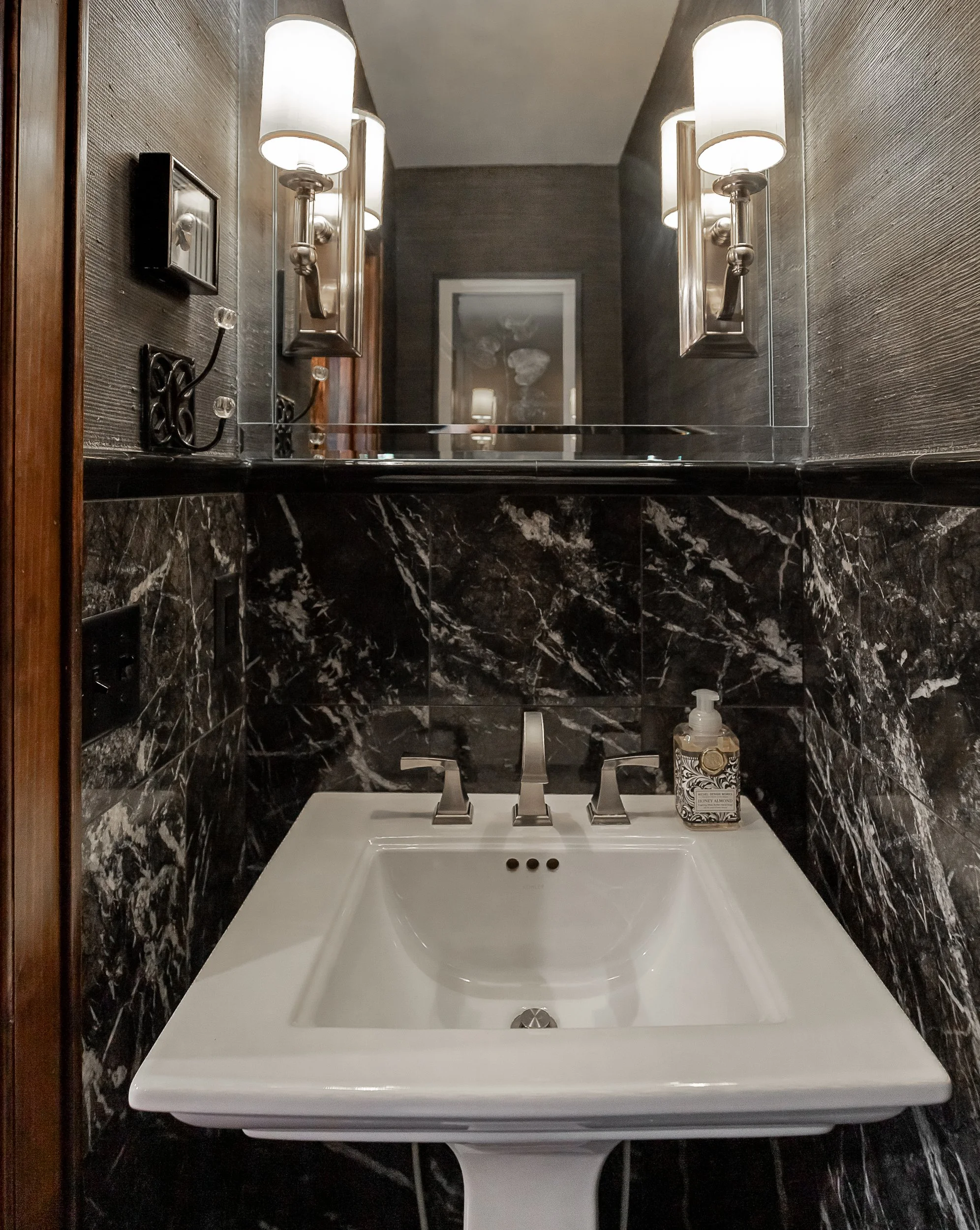 Bathroom sink with black marble walls, a large mirror, and modern light fixtures.