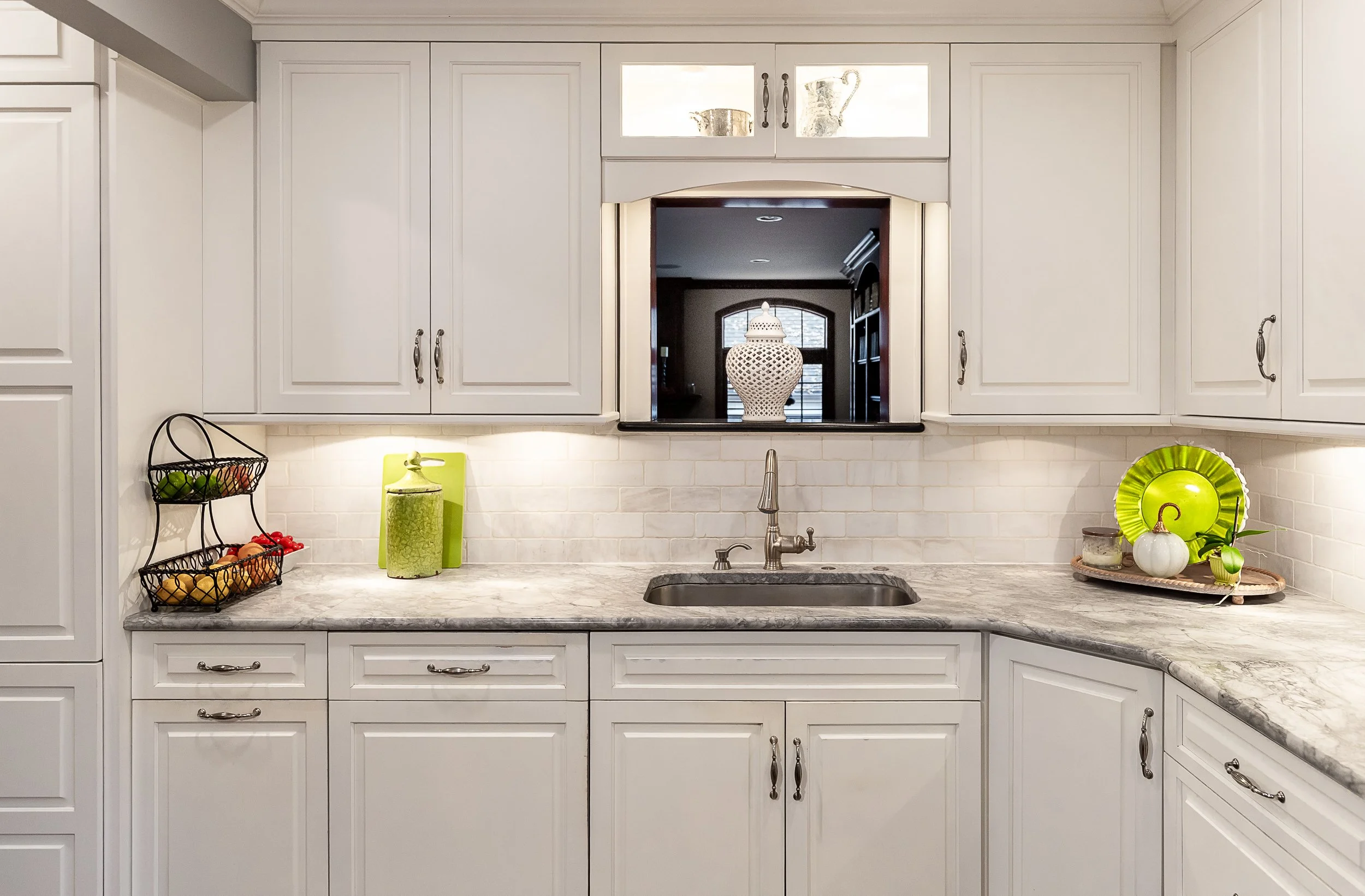 Kitchen with white cabinets, quartz countertop, and a window overhead with decorative items and greenery.