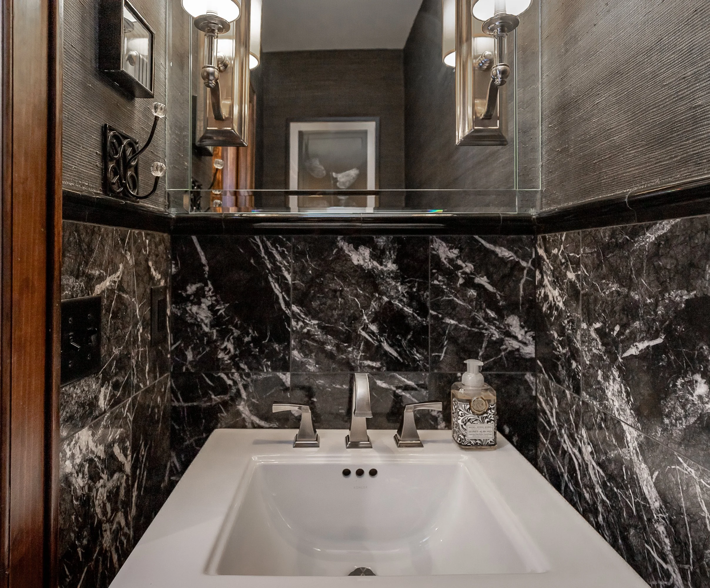 Bathroom with beige tiled walls, a vanity with a quartz countertop, a rectangular mirror, a three-light vanity fixture, a brass faucet, a shower with a brass showerhead, and a built-in tiled shelf in the shower area.