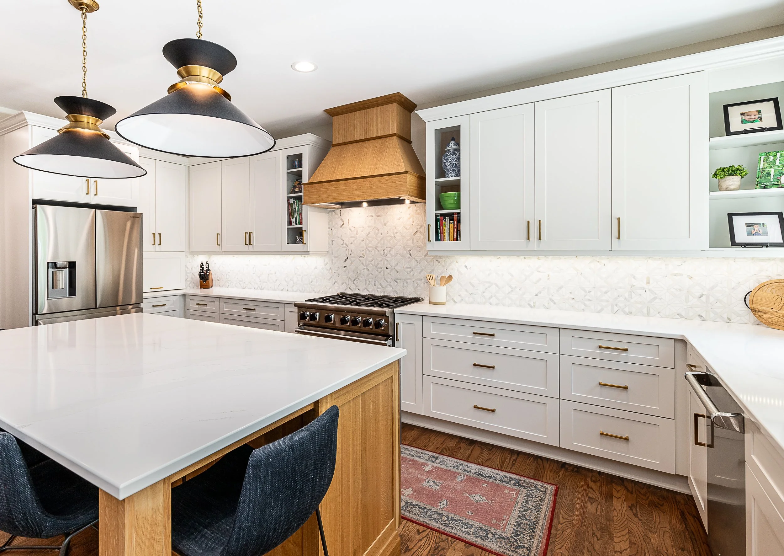Modern kitchen with white cabinets, a central island, stainless steel refrigerator, wooden range hood, and pendant lights.