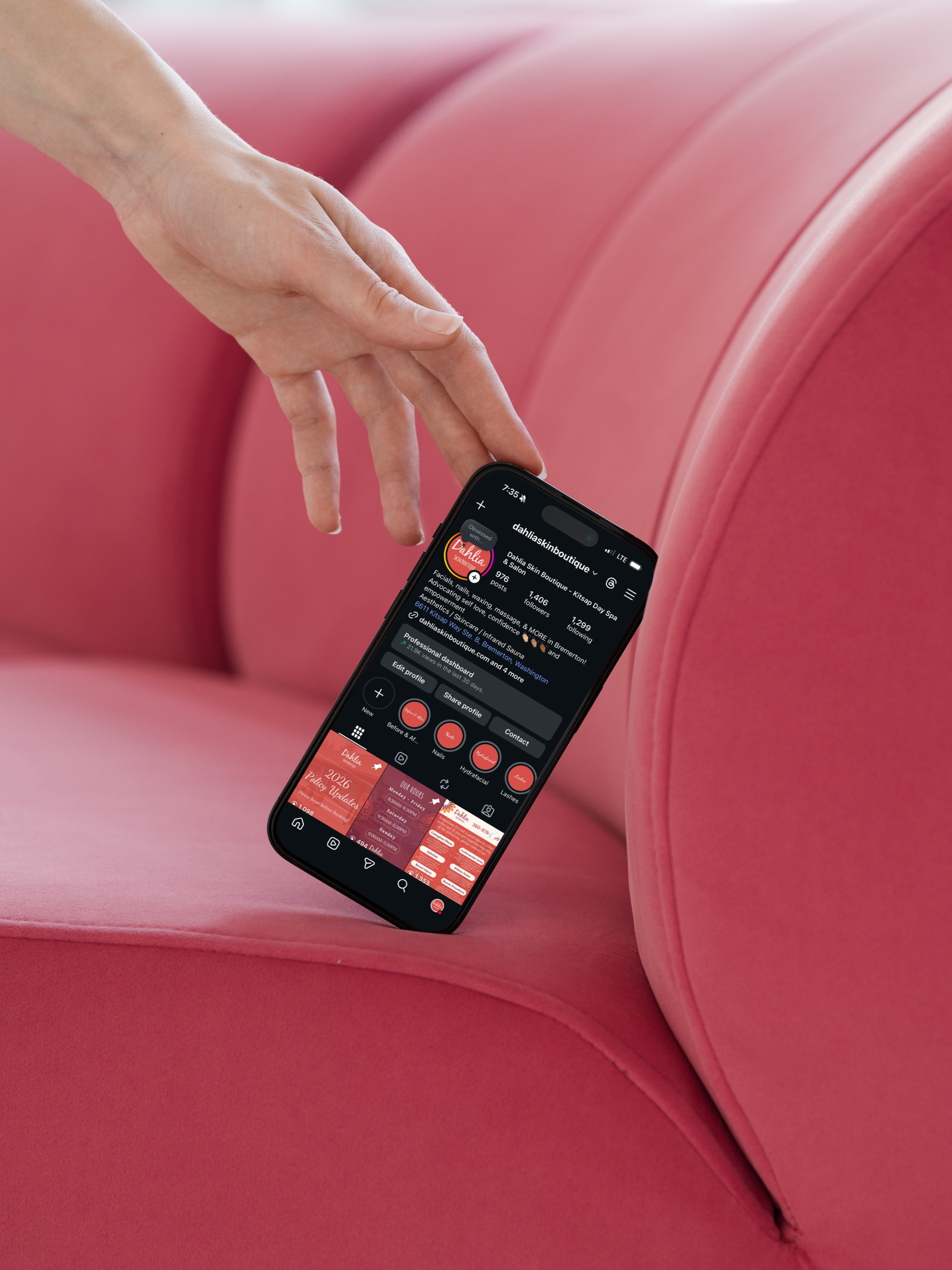 A hand holding a smartphone displaying an Instagram profile with pink-themed posts, resting on a pink upholstered surface.