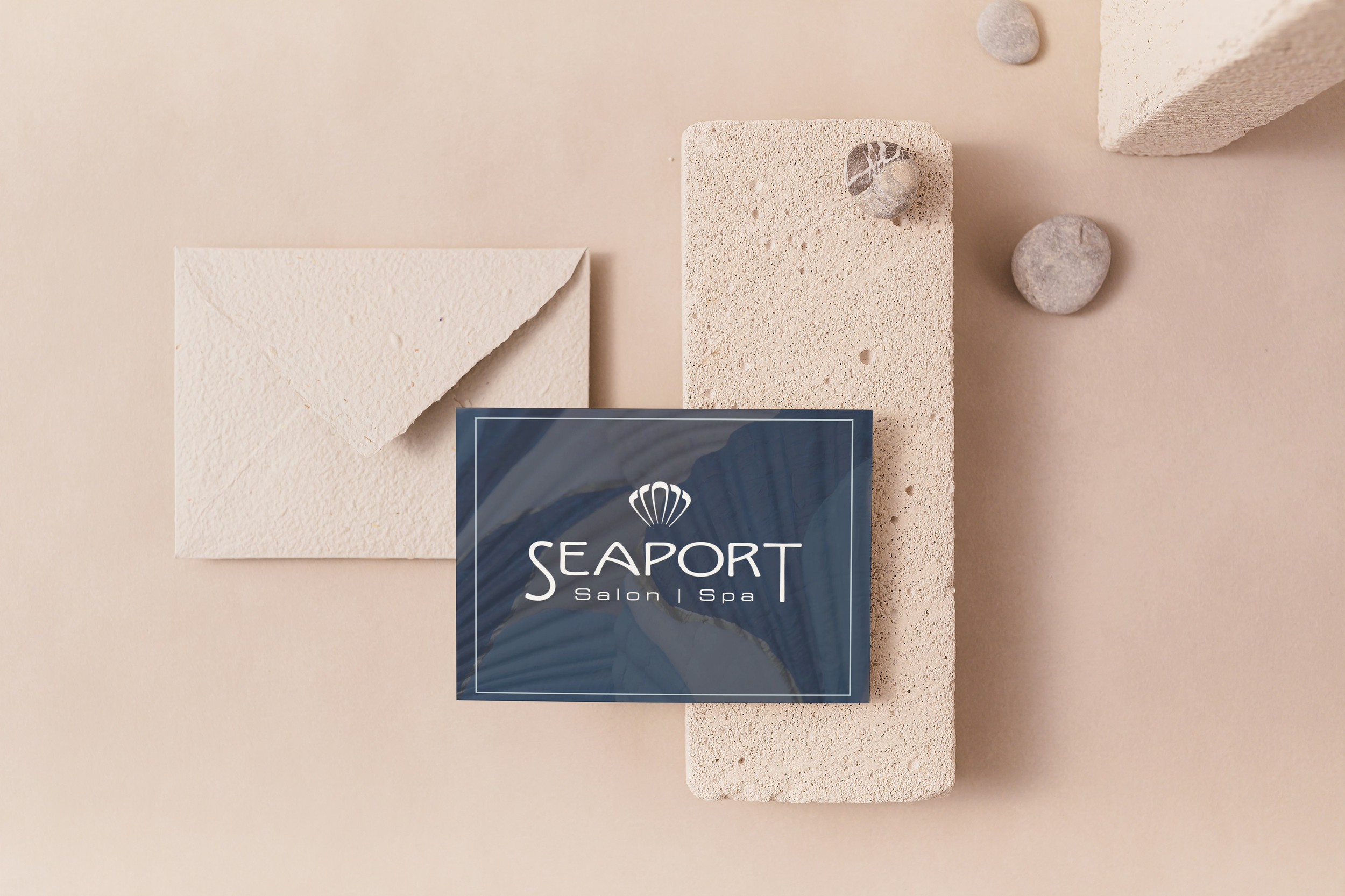 Arrangement of beige textured spa stones, a navy blue and white 'Seaport Salon | Spa' sign on a beige background with a soft, calming aesthetic.