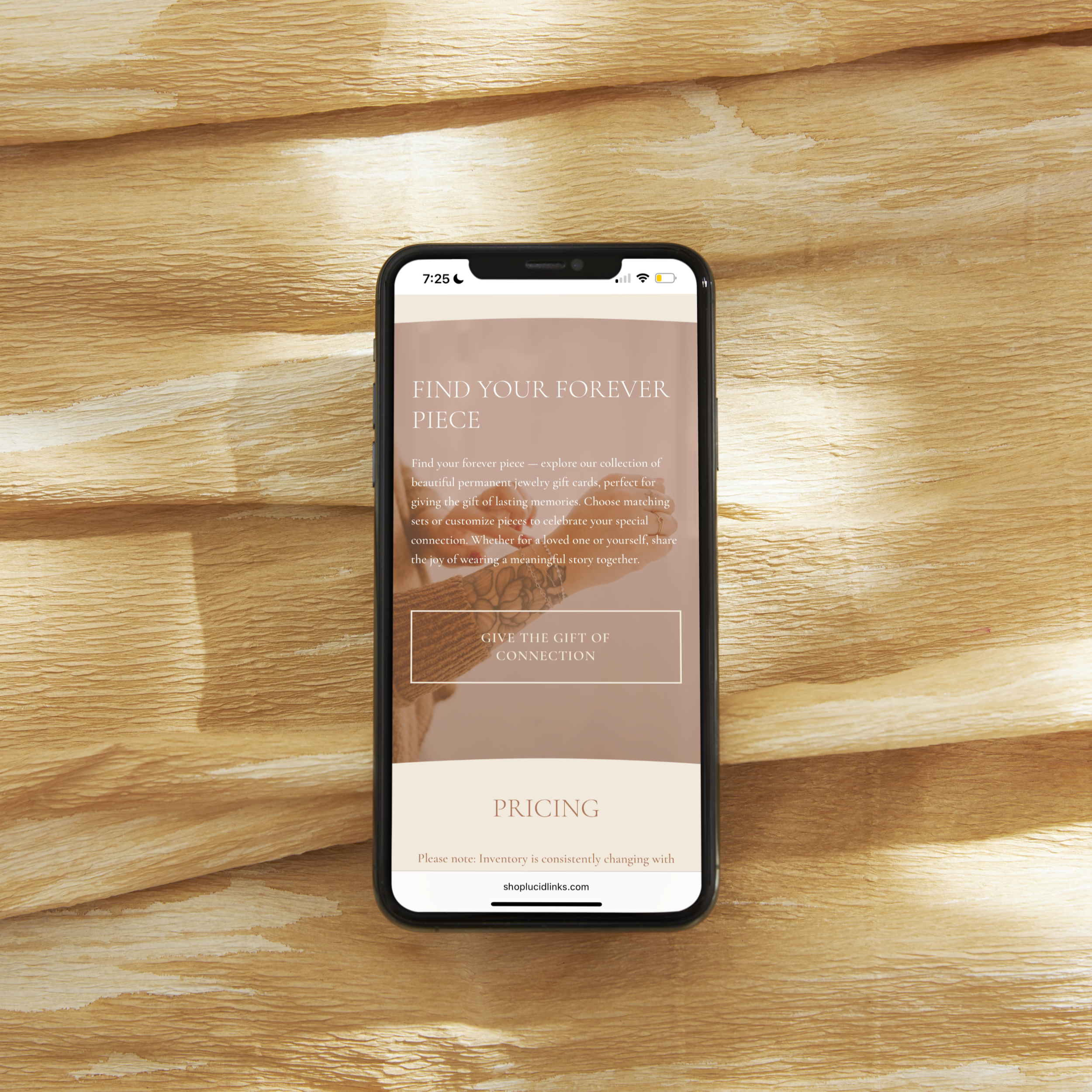 Smartphone on wooden surface displaying a jewelry website with text about finding a forever piece and pricing.