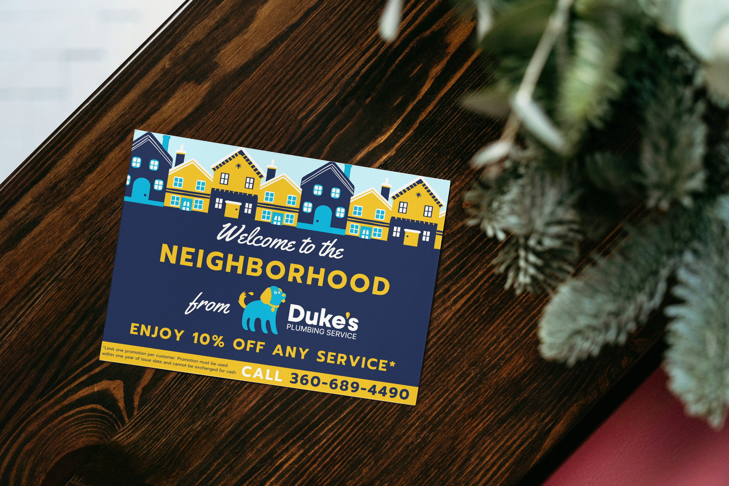 A flyer on a dark wood table promoting Duke's Plumbing Service, offering 10% off with a contact phone number, beside a partially visible Christmas tree.