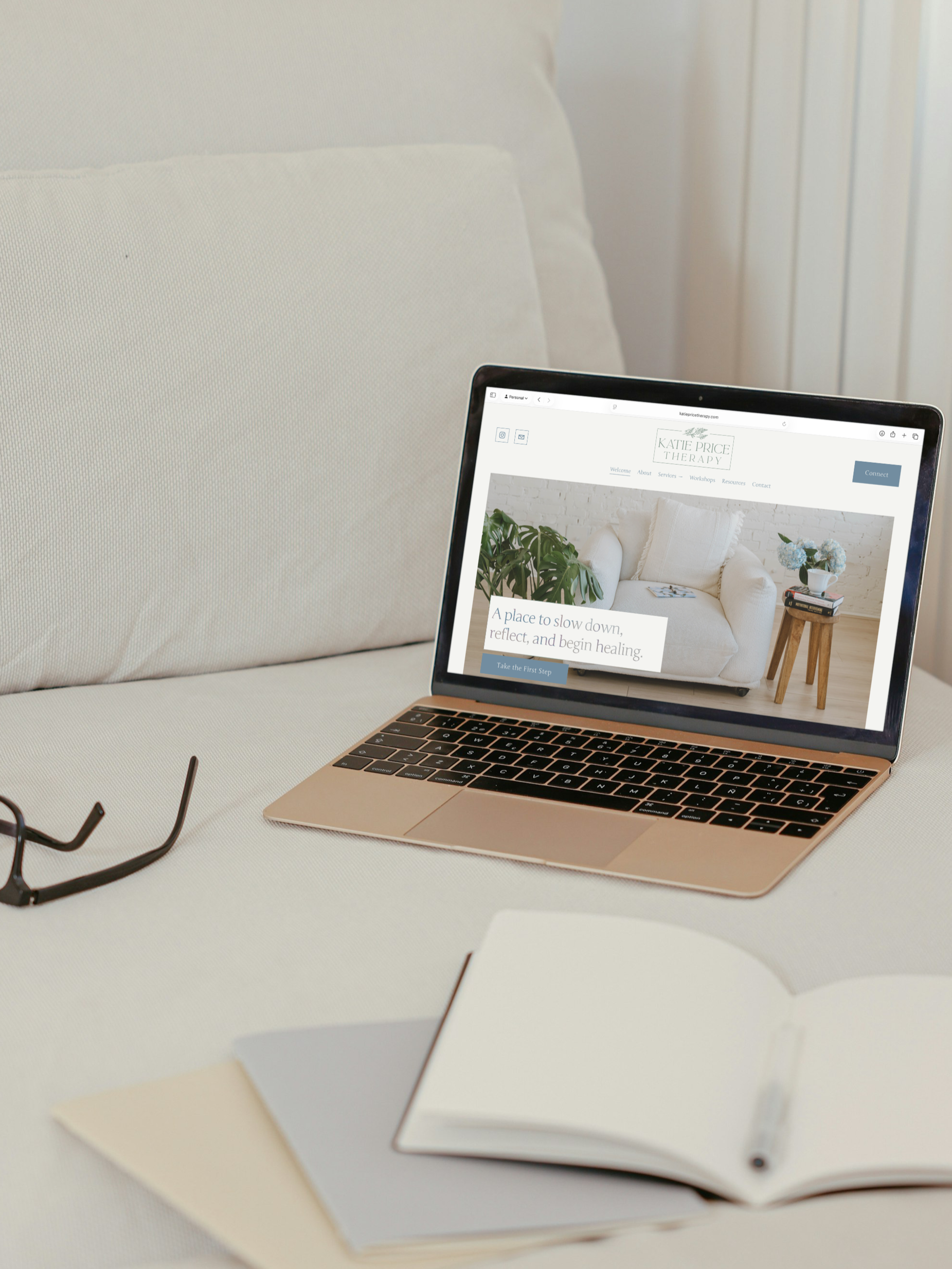 Open laptop on a white table displaying a therapy website, with glasses and notebooks nearby.