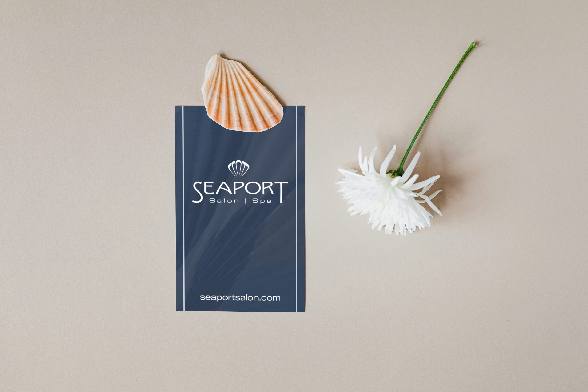 A navy blue promotional flyer for Seaport Salon and Spa with a seashell and a white flower attached to a beige background.