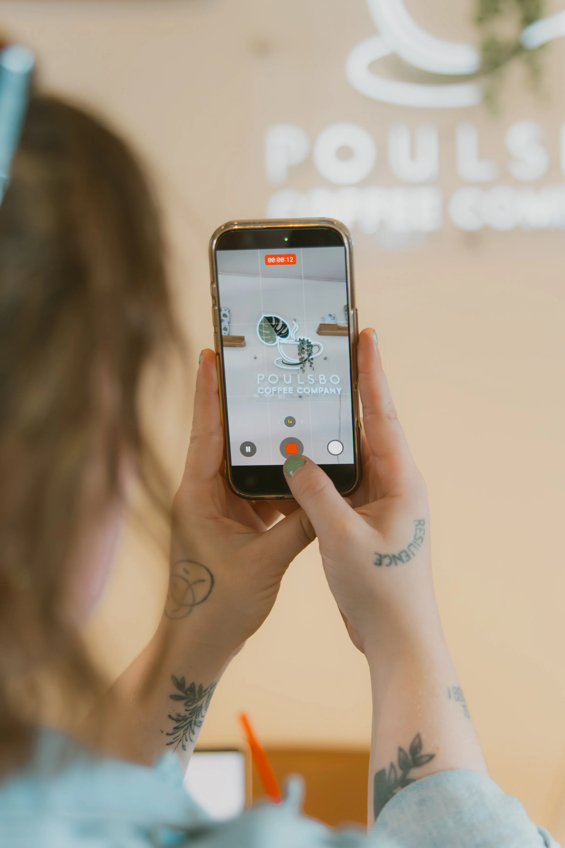 Person taking a photo of a coffee shop sign called Poulsbo Coffee Company with a smartphone in a cafe.