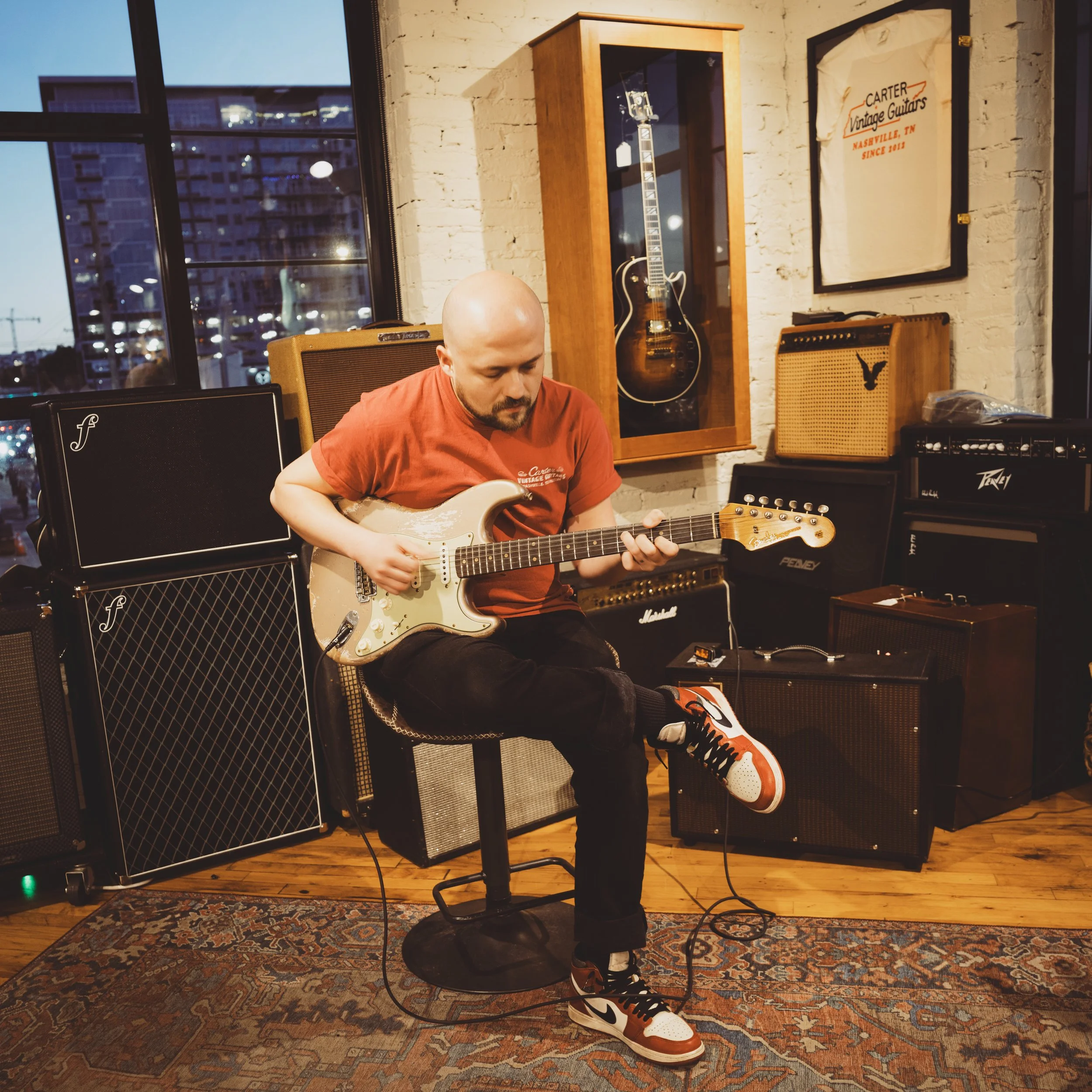 Man playing a beat-up Fender Stratocaster in front of several amps.