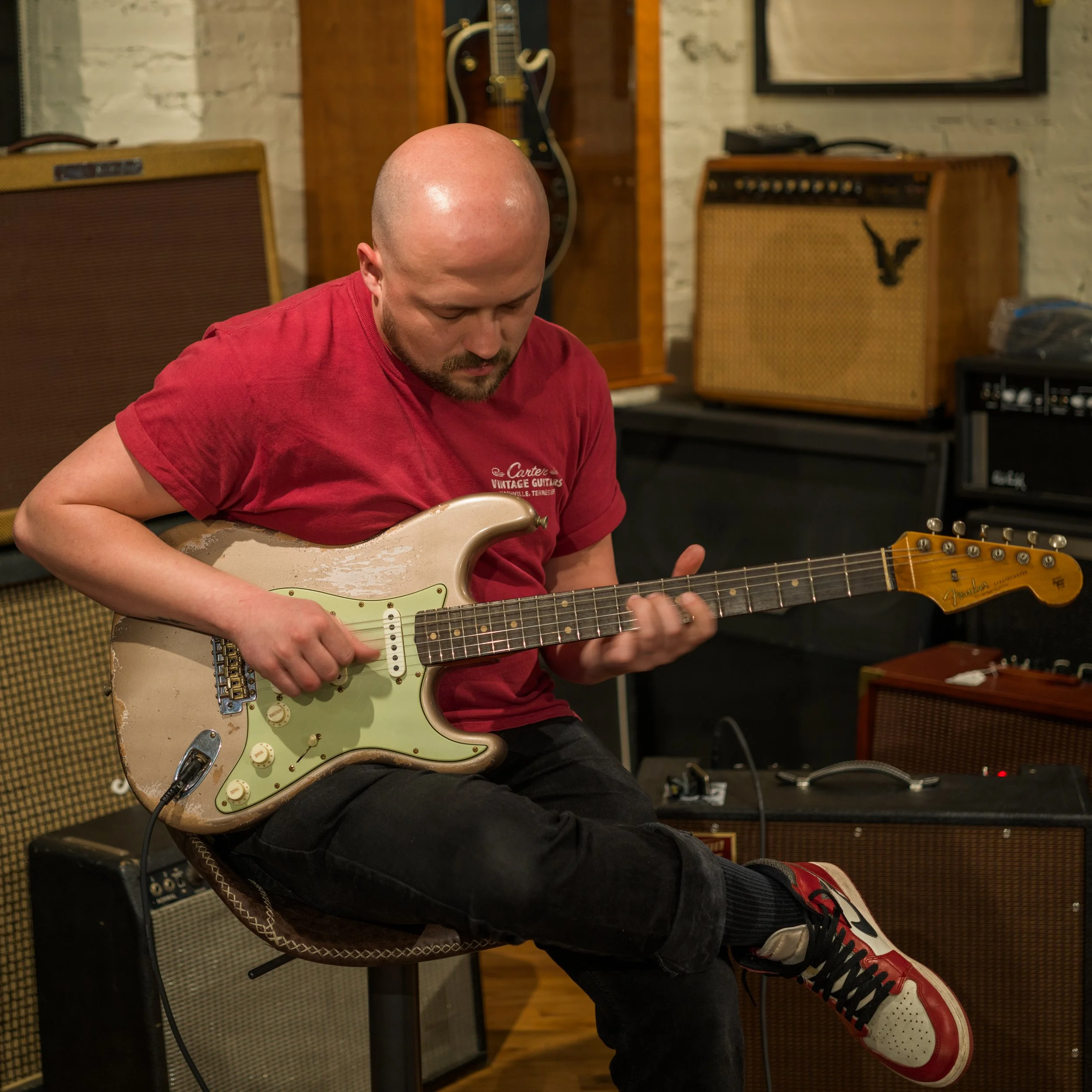 Close-up of a man playing a beat-up Fender Stratocaster guitar.