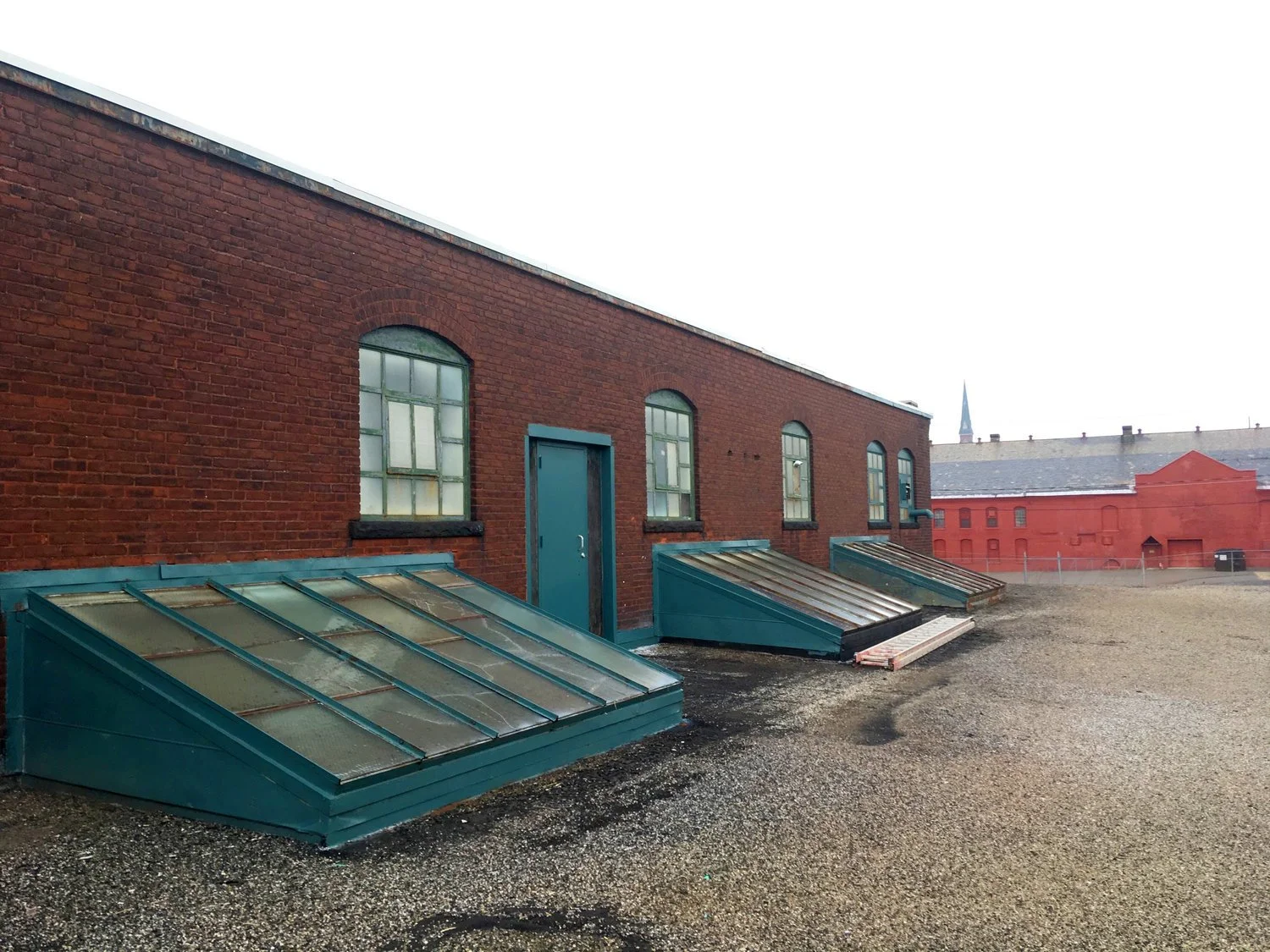 View of a rooftop with three glass skylights and a red brick building with arched windows.
