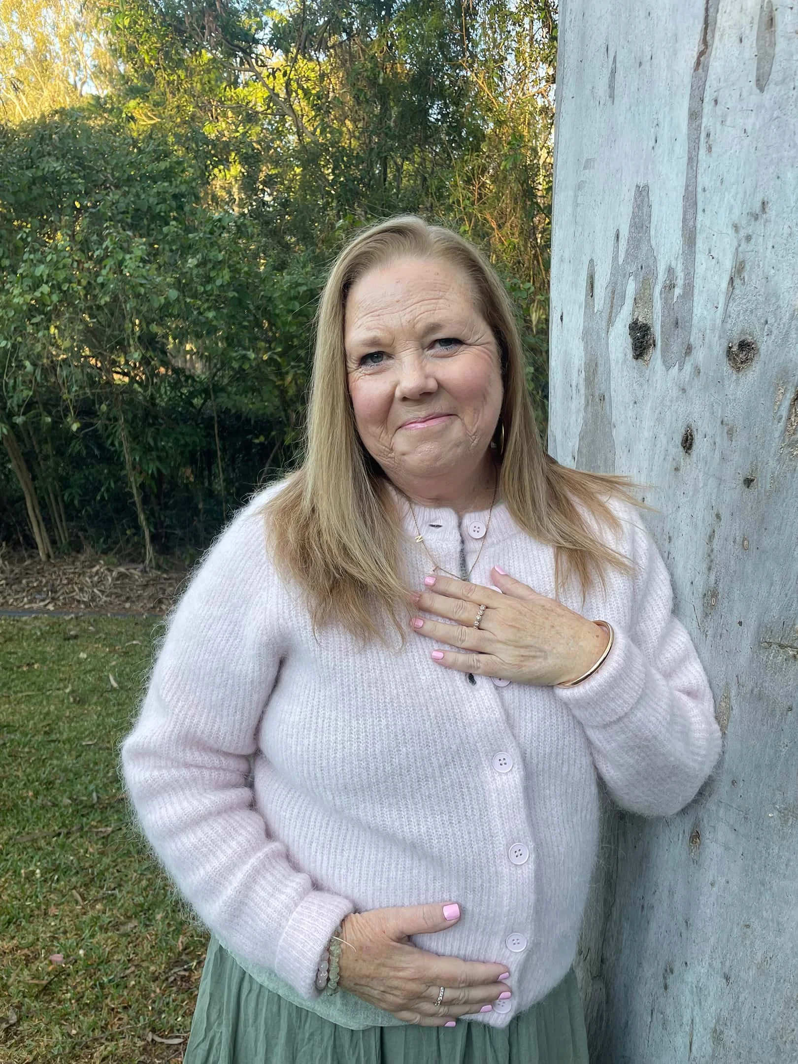 Kym Stewart, Reiki and intuitive guidance practitioner, leaning against a tree outdoors