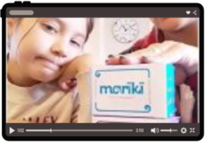 A young girl resting her head on a table with a Monki branded box in front of her, in a room with a clock on the wall.