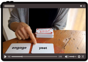 Person pointing at a card labeled 'engage' while holding a card labeled 'yeet' on a wooden table.