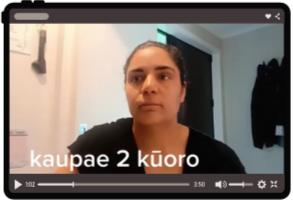 A woman with dark hair pulled back, sitting indoors with a neutral expression, in front of a door with a coat hanging on the wall.
