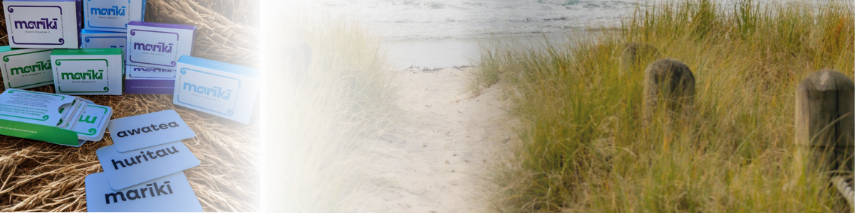 Image of educational flashcards with words in a language, set on a textured surface on the left side, and a sandy path with grass and weathered wooden posts on the right side.