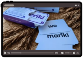 Flashcards with words 'wo' and 'mariki' on a wooden surface, with a purple and white box in the background.