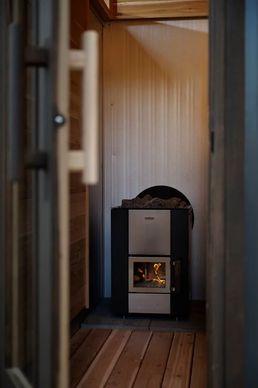 Wood-burning sauna heater seen through the open door of a Mettä sauna